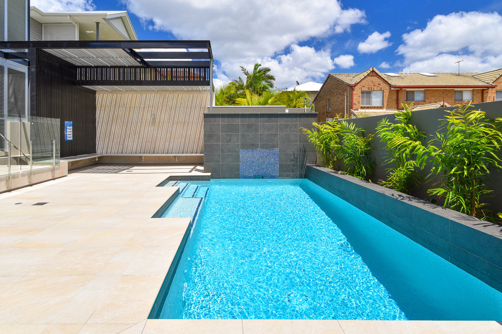Photo of a large modern back rectangular lengths swimming pool in Brisbane with a water feature and tiled flooring.
