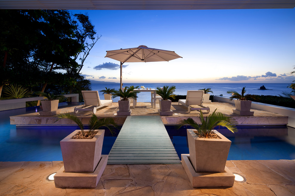 Immagine di una piscina a sfioro infinito tropicale personalizzata di medie dimensioni e dietro casa con fontane e pavimentazioni in pietra naturale