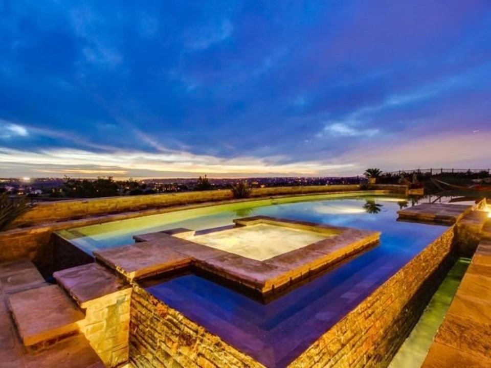 На фото: большой прямоугольный бассейн-инфинити на заднем дворе в средиземноморском стиле с джакузи и покрытием из каменной брусчатки