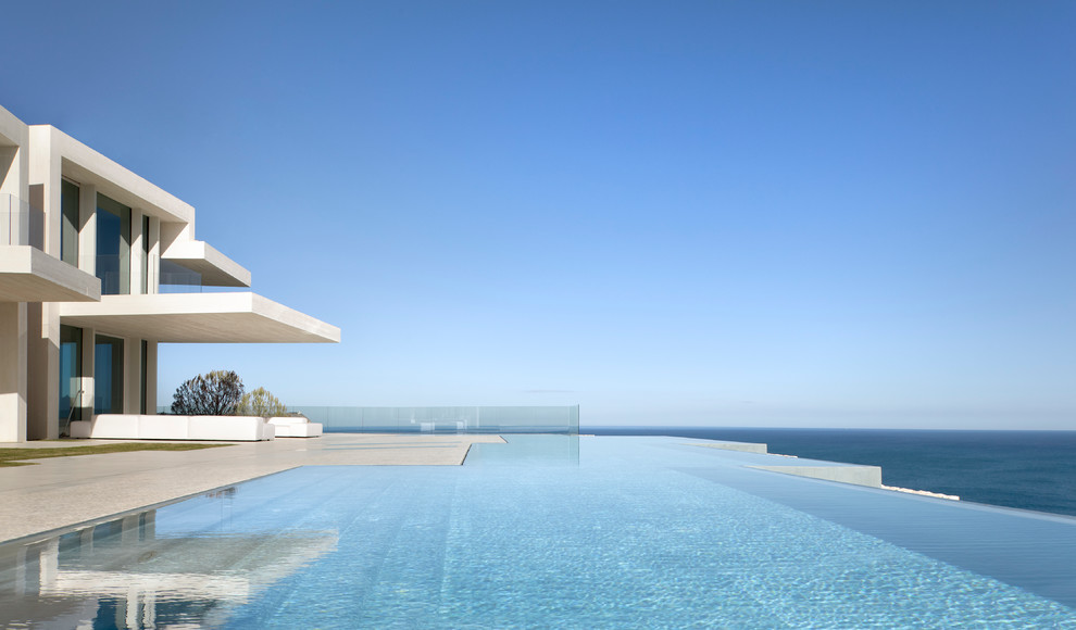 Ispirazione per un'ampia piscina a sfioro infinito contemporanea personalizzata dietro casa con lastre di cemento