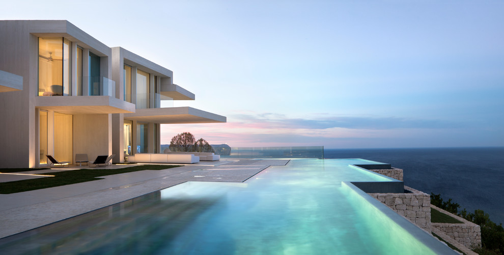 Idee per un'ampia piscina a sfioro infinito design personalizzata dietro casa con lastre di cemento