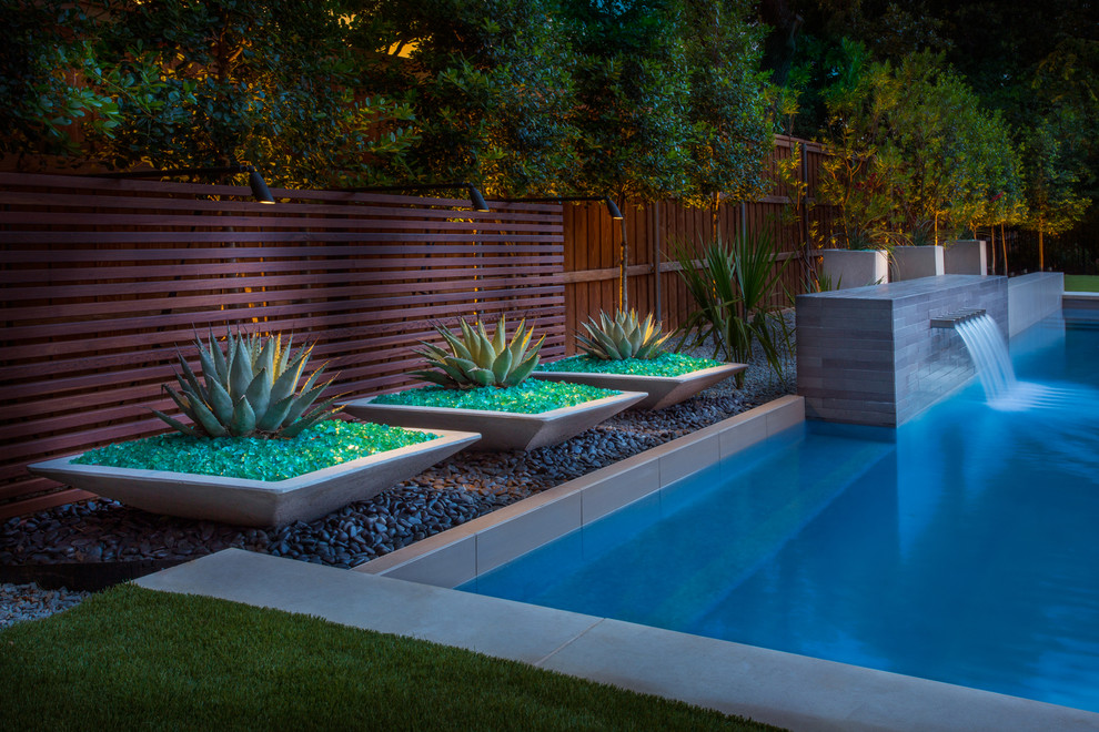 Diseño de piscina con fuente alargada actual rectangular en patio trasero con losas de hormigón