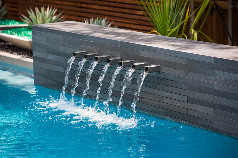 This is an example of a contemporary back rectangular lengths swimming pool in Dallas with a water feature and concrete slabs.