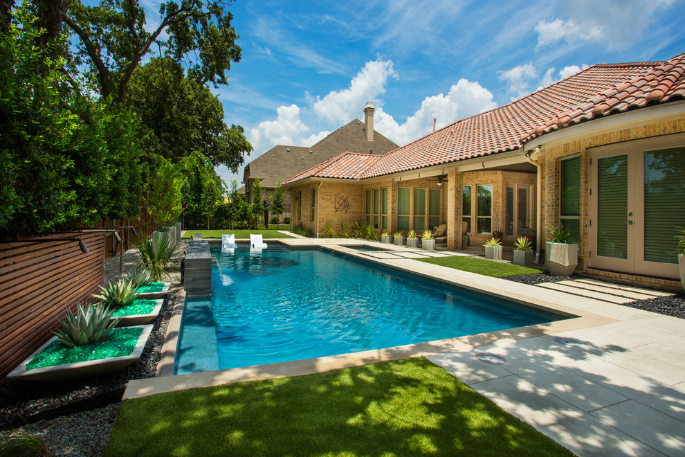 Ejemplo de piscina con fuente alargada actual rectangular en patio trasero con losas de hormigón