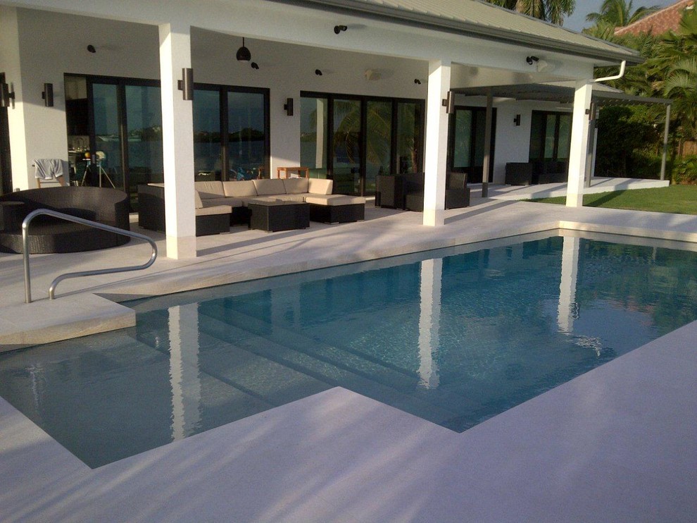 Idee per un'ampia piscina naturale tropicale rettangolare dietro casa con una vasca idromassaggio e lastre di cemento