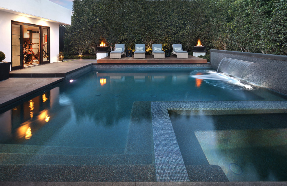 Modelo de piscinas y jacuzzis grandes rectangulares en patio trasero con adoquines de piedra natural