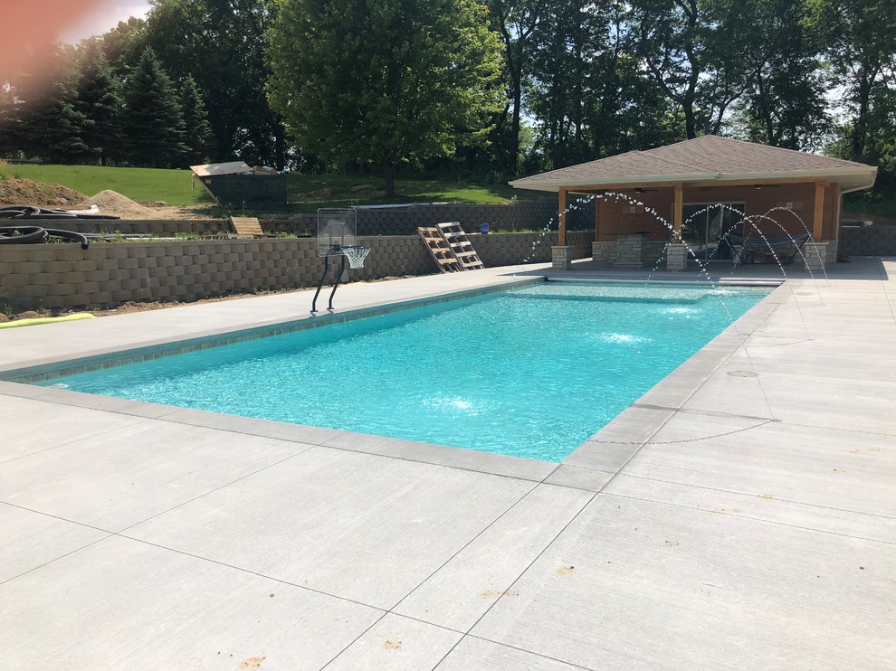Inspiration for a large traditional back rectangular lengths swimming pool in Cedar Rapids with concrete slabs and a water feature.