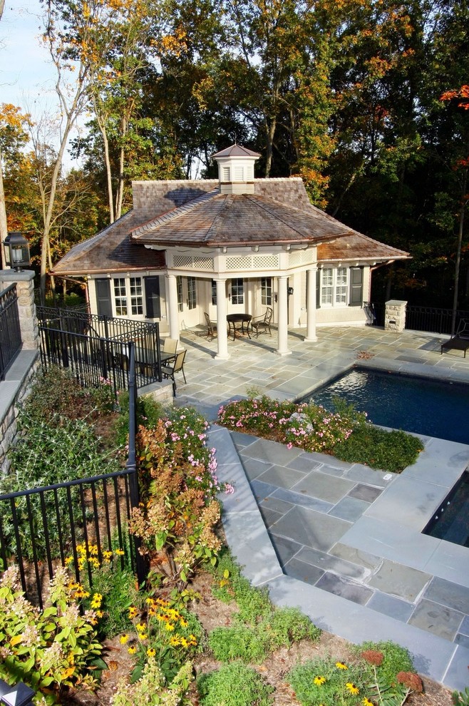 Foto på en stor träningspool på baksidan av huset, med poolhus och naturstensplattor