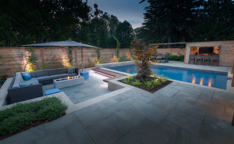 Ejemplo de casa de la piscina y piscina actual grande rectangular en patio trasero con adoquines de piedra natural