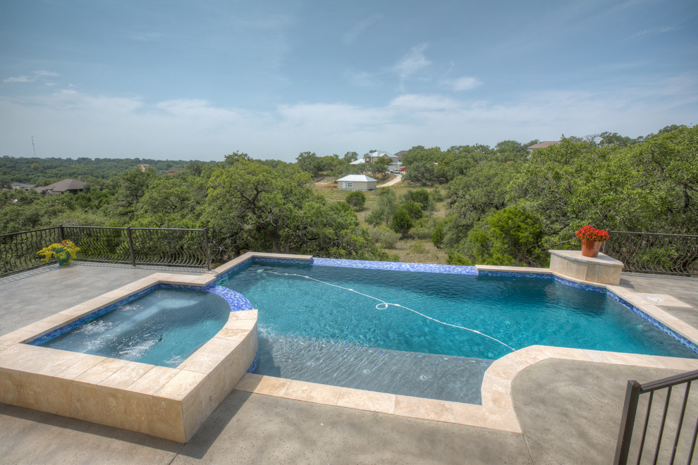 На фото: большой прямоугольный бассейн-инфинити на заднем дворе в средиземноморском стиле с джакузи и покрытием из бетонных плит