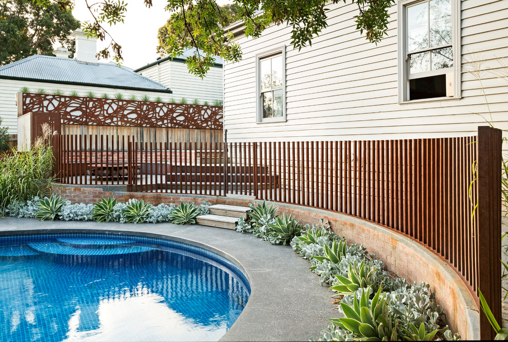 Ejemplo de piscina minimalista de tamaño medio redondeada en patio lateral con losas de hormigón