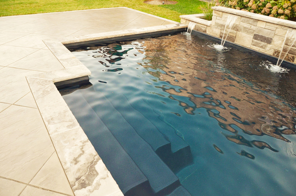 Réalisation d'une piscine arrière tradition de taille moyenne et rectangle avec des pavés en pierre naturelle.