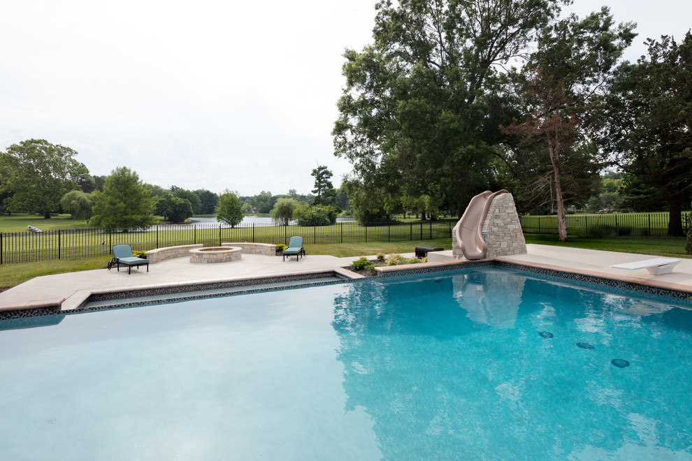 Modelo de piscina con tobogán infinita campestre grande rectangular en patio trasero con suelo de hormigón estampado