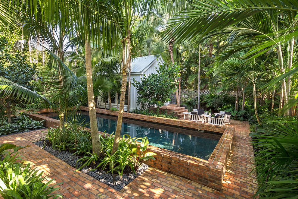 Modelo de piscina tropical de tamaño medio rectangular en patio trasero con adoquines de ladrillo