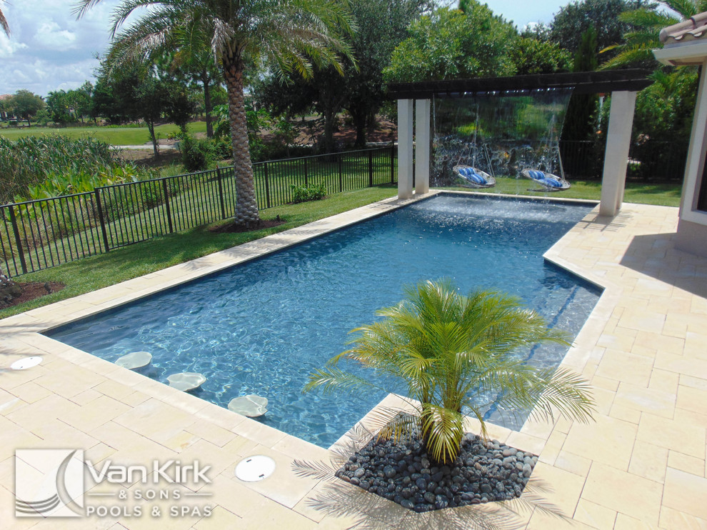 Cette image montre une grande piscine naturelle et arrière design rectangle avec un point d'eau et des pavés en pierre naturelle.