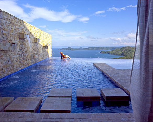 Imagen de piscina con fuente infinita moderna extra grande en forma de L en patio trasero con adoquines de ladrillo