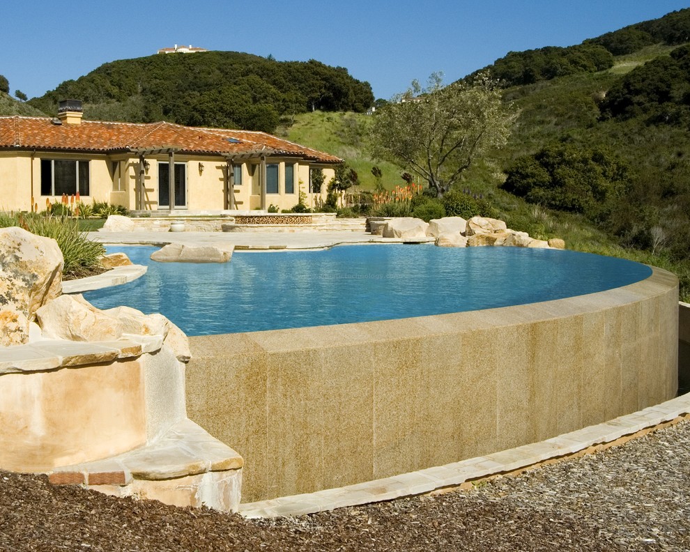 Immagine di un'ampia piscina a sfioro infinito mediterranea personalizzata dietro casa con pavimentazioni in pietra naturale e una vasca idromassaggio