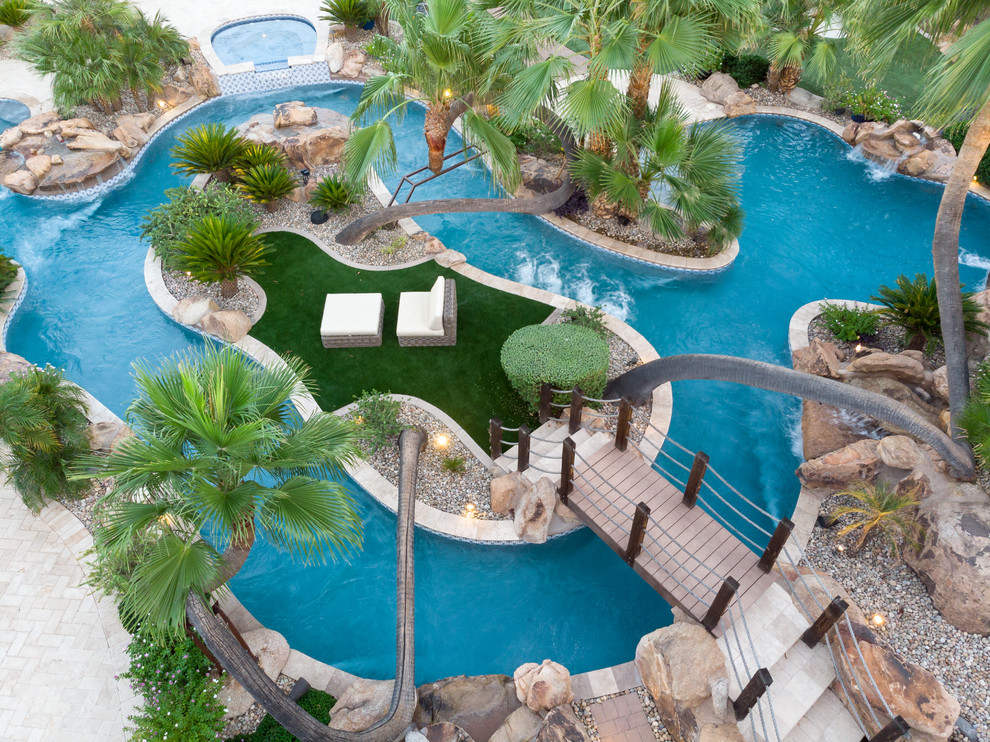 Idee per una grande piscina tropicale personalizzata dietro casa con un acquascivolo e pavimentazioni in pietra naturale