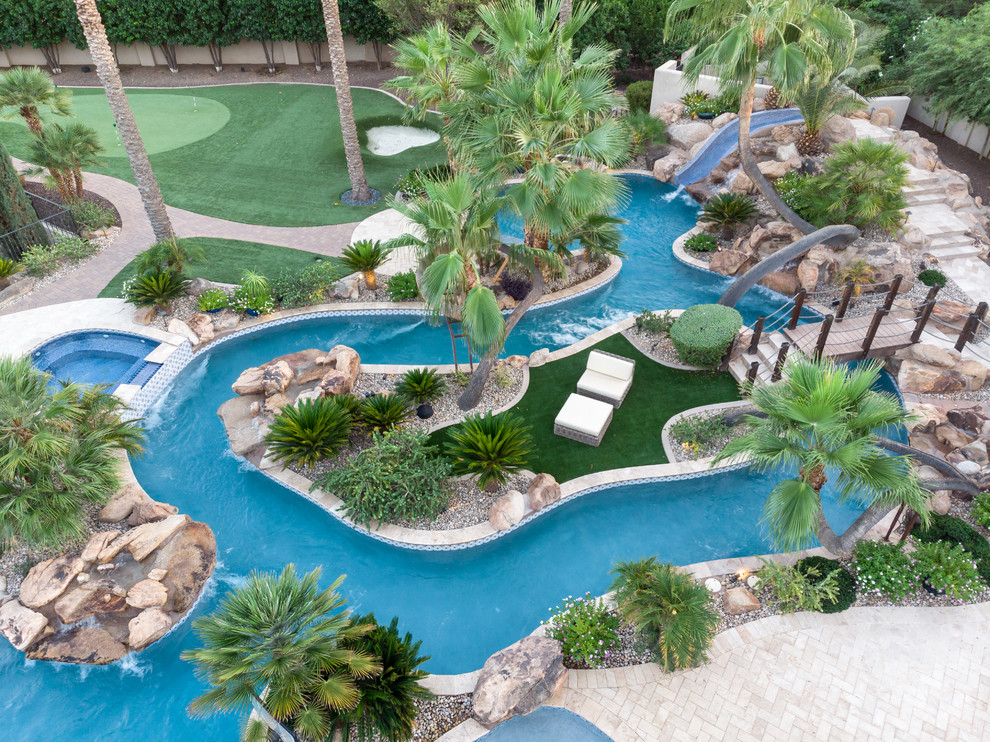 Large world-inspired back custom shaped swimming pool in Phoenix with a water slide and natural stone paving.