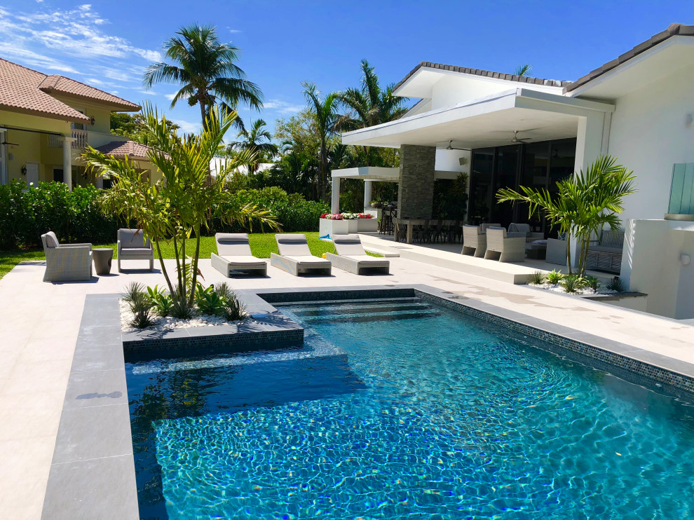Diseño de piscina natural actual extra grande rectangular en patio trasero con adoquines de piedra natural