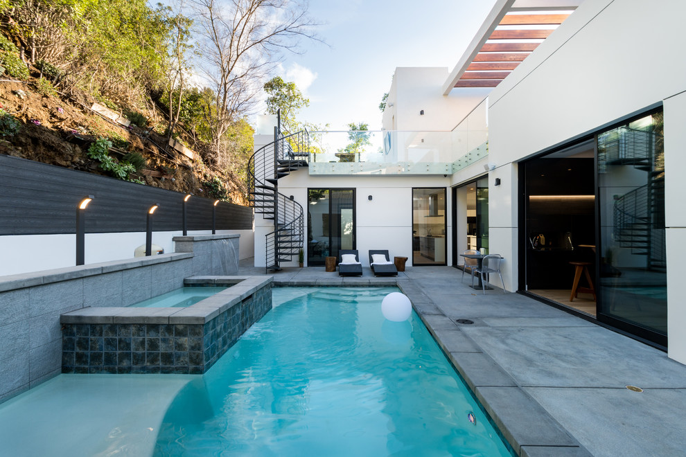 Modelo de piscina alargada contemporánea rectangular en patio trasero con losas de hormigón