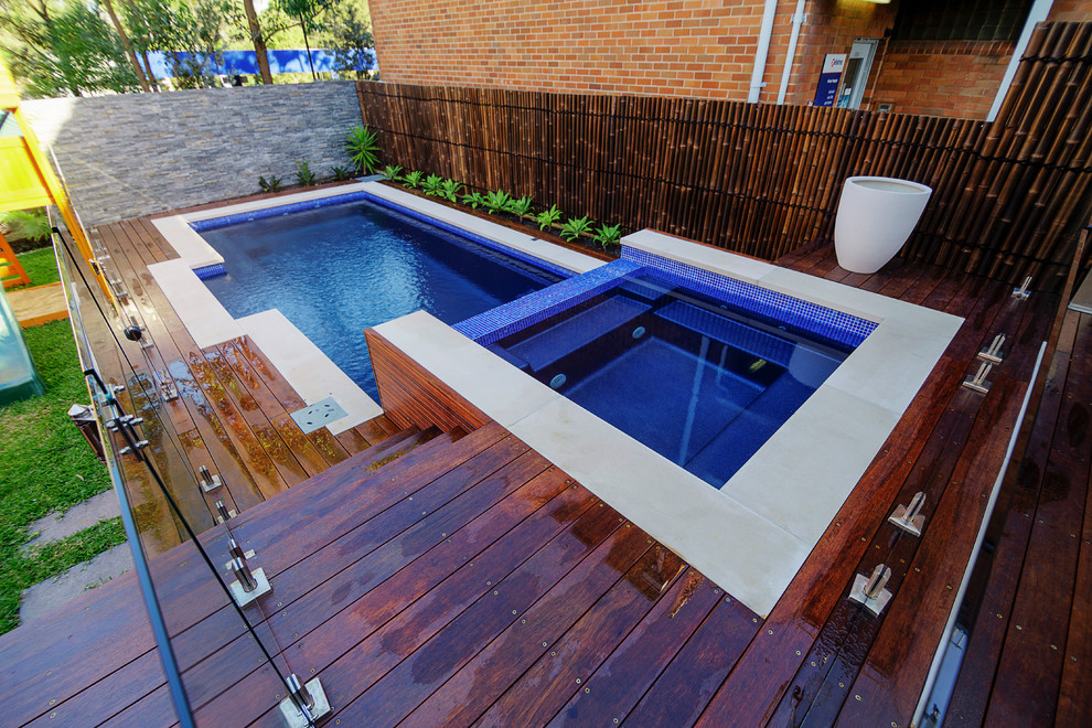 Réalisation d'une piscine arrière design de taille moyenne et rectangle avec un bain bouillonnant et une terrasse en bois.