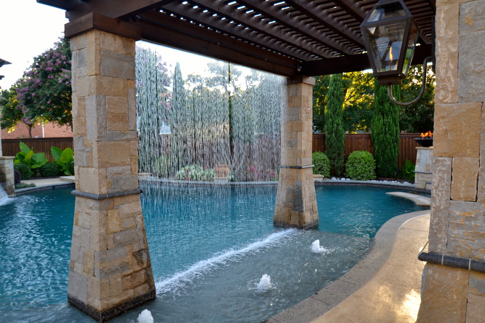 Large classic back custom shaped swimming pool in Dallas with stamped concrete and a water feature.
