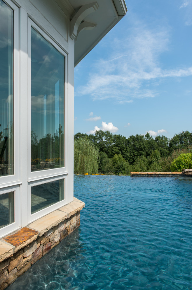 Example of a mid-sized classic backyard stone and custom-shaped infinity pool fountain design in Other