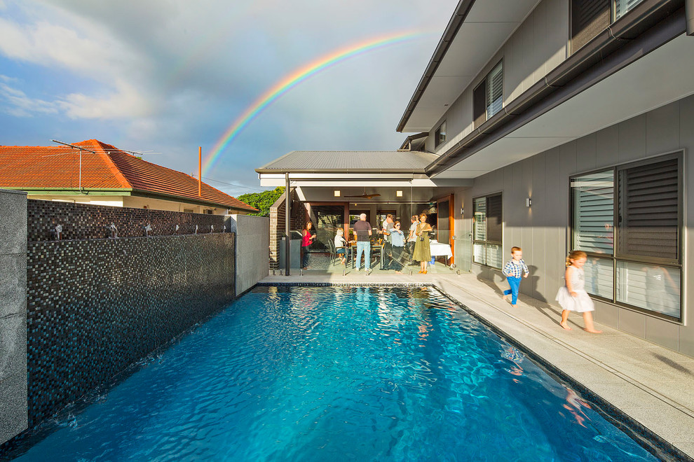 Imagen de piscina con fuente natural actual de tamaño medio rectangular en patio trasero con suelo de baldosas