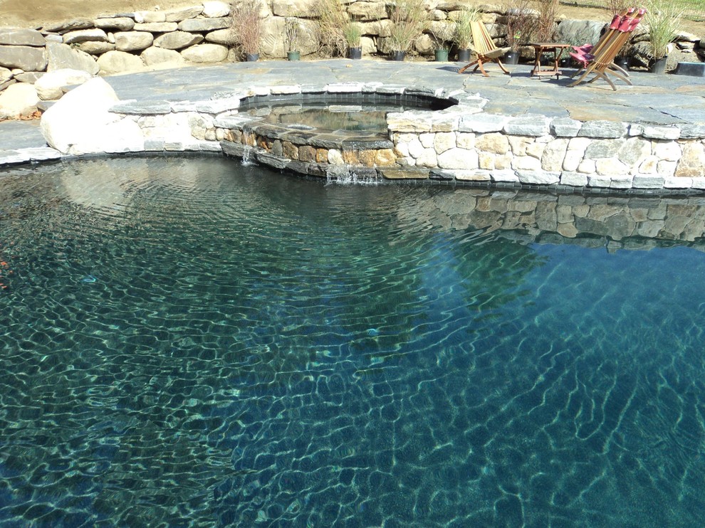 Cette image montre une très grande piscine naturelle et arrière rustique en forme de haricot avec un bain bouillonnant et des pavés en pierre naturelle.