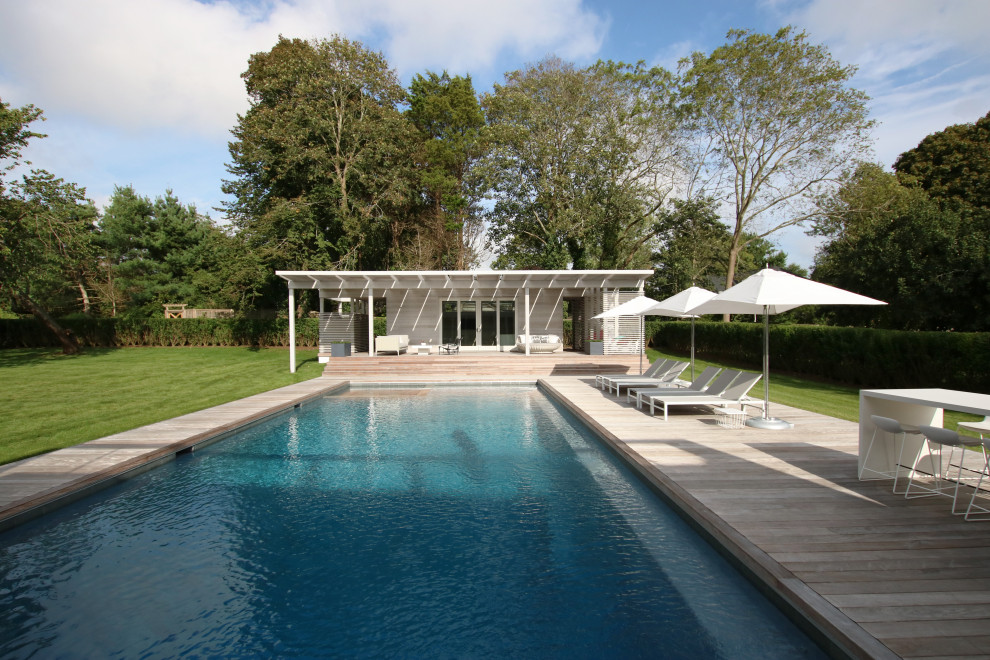 Modern inredning av en stor rektangulär pool på baksidan av huset, med poolhus och trädäck
