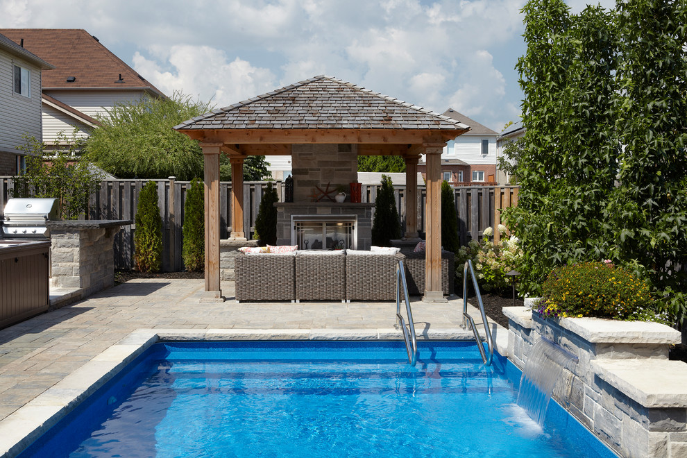 This is an example of a small contemporary back rectangular natural swimming pool in Toronto with a water feature and brick paving.