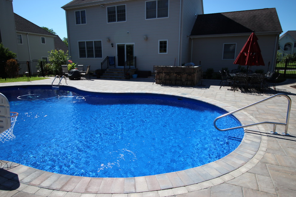 Diseño de piscina natural tradicional grande a medida en patio trasero con adoquines de hormigón