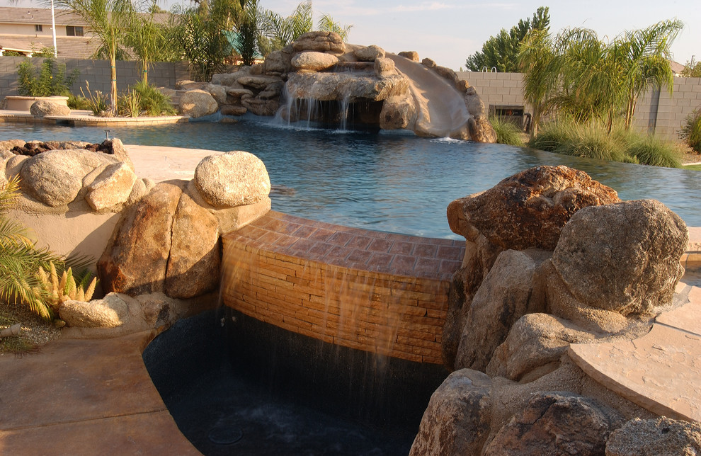 Photo of a large modern back custom shaped infinity swimming pool in Phoenix with a water feature and stamped concrete.