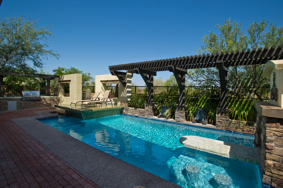 Design ideas for a large modern back custom shaped infinity swimming pool in Phoenix with a water feature and brick paving.