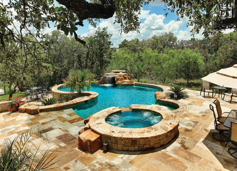 Réalisation d'une grande piscine arrière design sur mesure avec un point d'eau et des pavés en pierre naturelle.