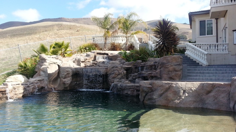 Idée de décoration pour une grande piscine arrière et à débordement design sur mesure avec un toboggan et des pavés en pierre naturelle.