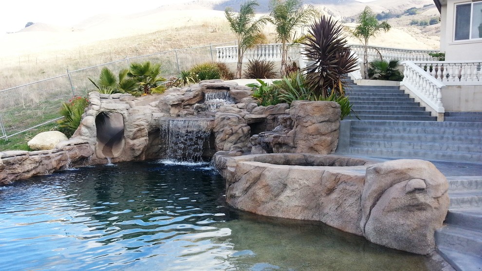 Design ideas for a large contemporary back custom shaped infinity swimming pool in San Francisco with a water slide and natural stone paving.