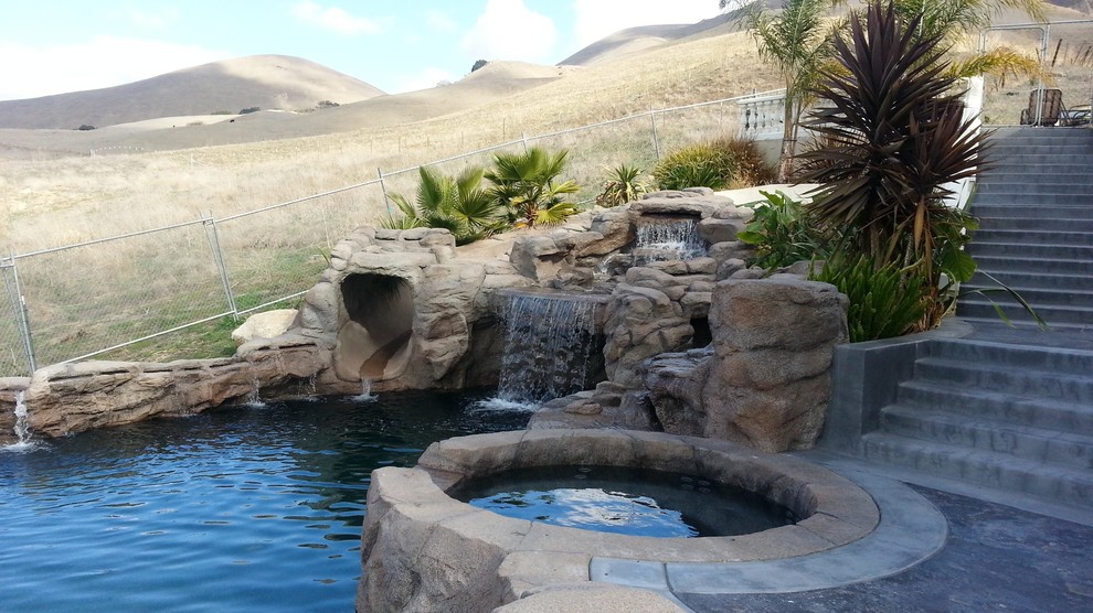 Imagen de piscina con tobogán infinita contemporánea grande a medida en patio trasero con adoquines de piedra natural