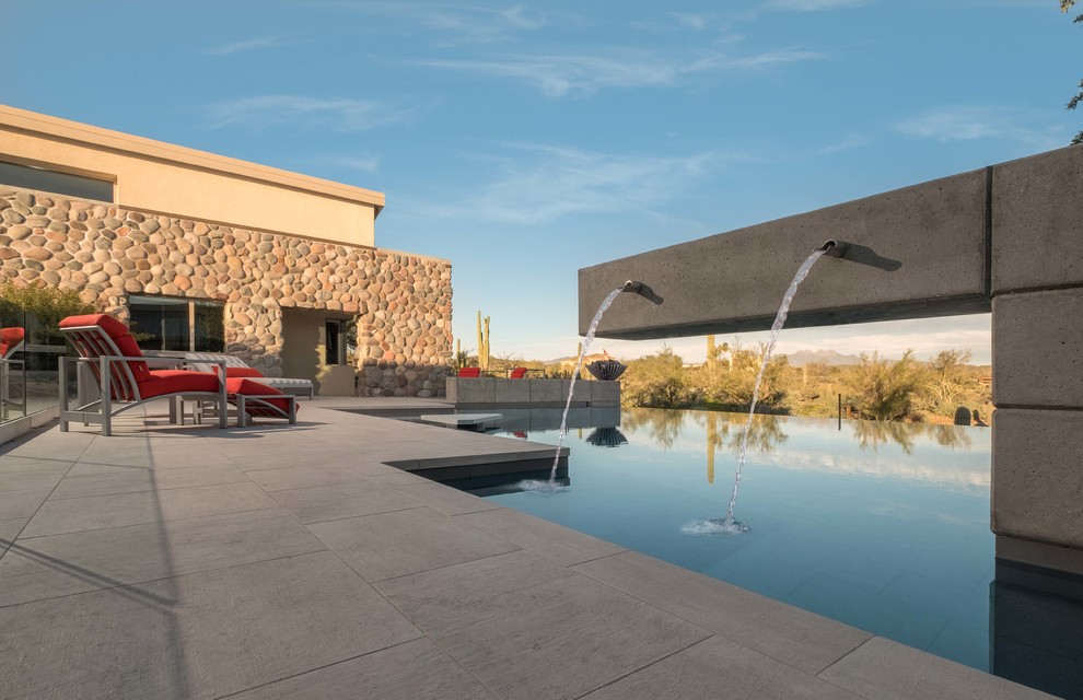 Diseño de piscina con fuente infinita actual grande a medida en patio trasero con suelo de baldosas