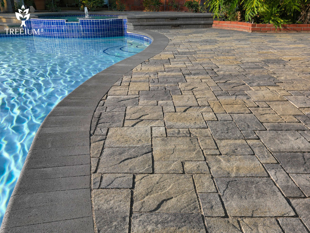 Diseño de piscina tropical grande en forma de L en patio trasero con adoquines de piedra natural