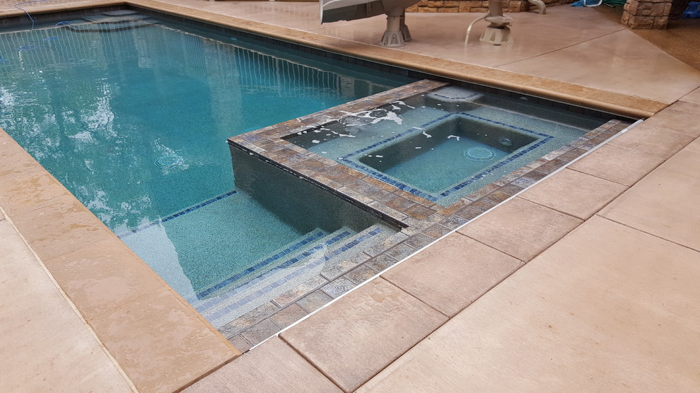 Immagine di una piscina classica rettangolare di medie dimensioni e dietro casa con una vasca idromassaggio e lastre di cemento