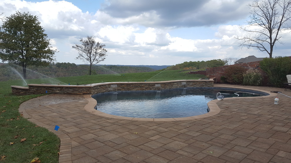 Medium sized classic back custom shaped natural swimming pool in Other with a water feature and concrete paving.