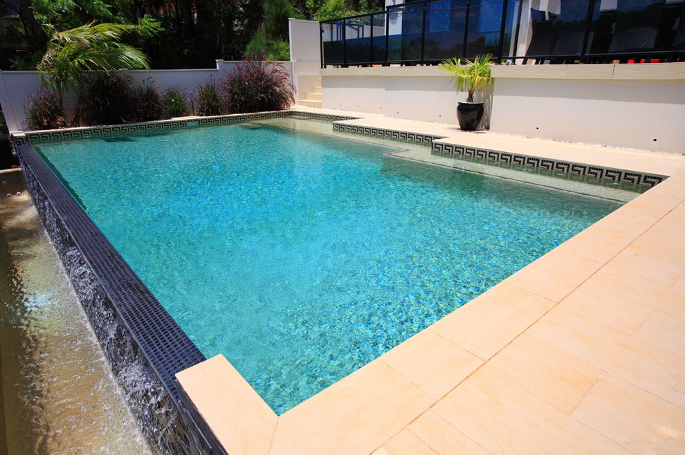 Esempio di una piscina a sfioro infinito design rettangolare di medie dimensioni e dietro casa con pavimentazioni in cemento