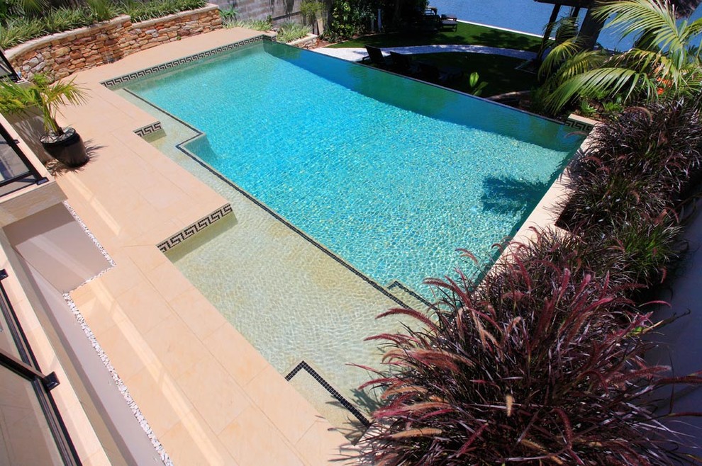Diseño de piscina infinita actual de tamaño medio rectangular en patio trasero con adoquines de hormigón