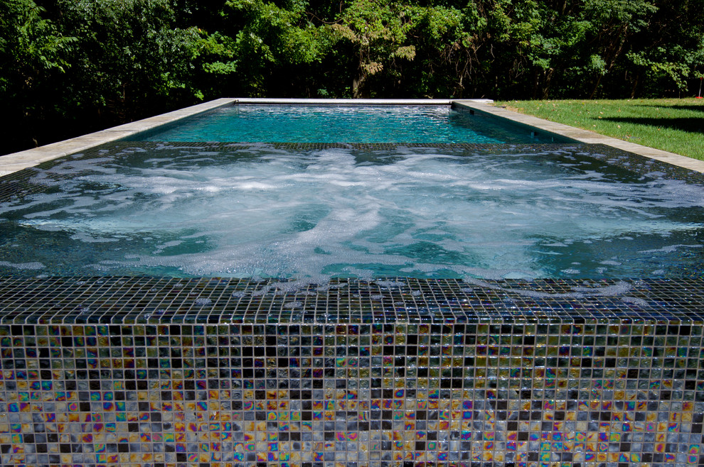 Ejemplo de piscinas y jacuzzis infinitos actuales de tamaño medio rectangulares en patio trasero con adoquines de piedra natural
