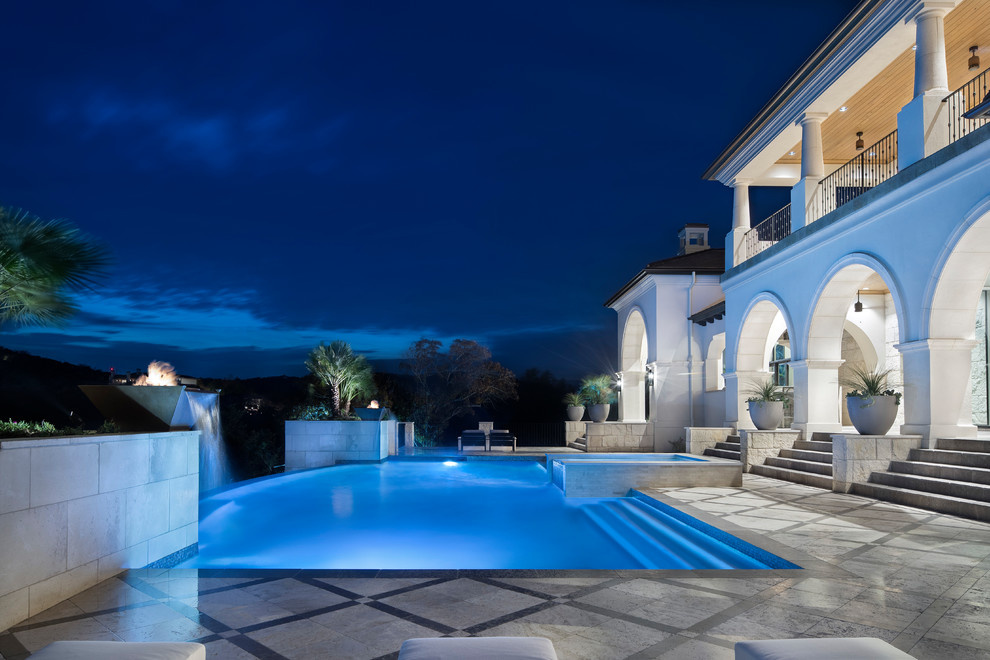 Foto di un'ampia piscina a sfioro infinito minimal rettangolare dietro casa con fontane e pavimentazioni in pietra naturale