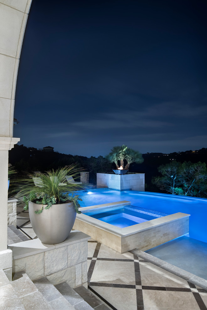 Immagine di un'ampia piscina a sfioro infinito design rettangolare dietro casa con una vasca idromassaggio e pavimentazioni in pietra naturale