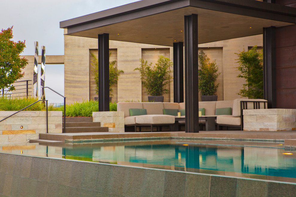 Idee per un'ampia piscina a sfioro infinito minimalista personalizzata dietro casa con fontane e lastre di cemento