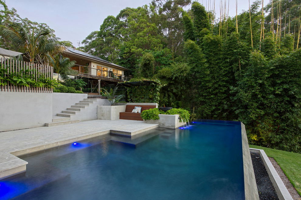 Diseño de piscina infinita actual grande a medida en patio trasero con adoquines de piedra natural
